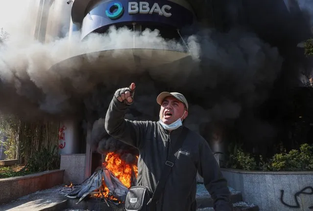 A demonstrator gestures near a bank, set on fire, during a protest organized by Depositors' Outcry, a group campaigning for angry depositors, against informal restrictions on cash withdrawals and deteriorating economic conditions in Beirut, Lebanon on February 16, 2023. (Photo by Mohamed Azakir/Reuters)