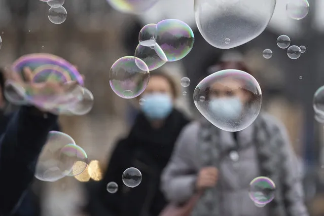 Soap bubbles float through the city centre of Stuttgart, Germany, Friday, December11, 2020. In the background, passers-by walk with mouth-nose protection. (Photo by Sebastian Gollnow/dpa via AP Photo)