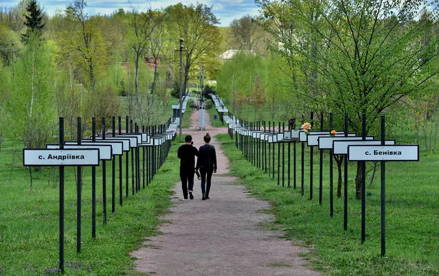 A couple of tourists walk in a symbolic alley with signs bearing names of villages and cities which were evacuated following the Chernobyl disaster during their tour of the exclusion zone on April 23, 2018. (Photo by Sergei Supinsky/AFP Photo)