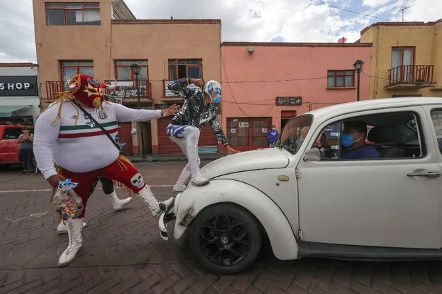 Mexican Lucha Libre wrestlers Mr. Jerry and Gran Felipe Jr. stop a car to hand out masks to their passengers as part of a local campaign to promote the use of face masks as a preventive measure against coronavirus on September 03, 2020 in Xochimilco, Mexico. Mexican wrestlers members of the wrestling show “Chinampaluchas” are part of a campaign promoted by local government to raise awareness on use of face masks to prevent spread of COVID-19. Wrestlers walk looking for people without face masks then simulate a fight and share a mask with them. (Photo by Hector Vivas/Getty Images)