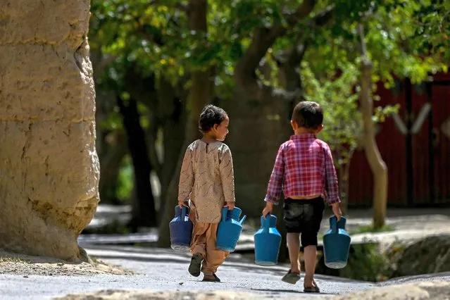 Afghan children carry water in a pitcher as they walk along a road in Tilanchi village of Parwan province on August 3, 2023. (Photo by Wakil Kohsar/AFP Photo)