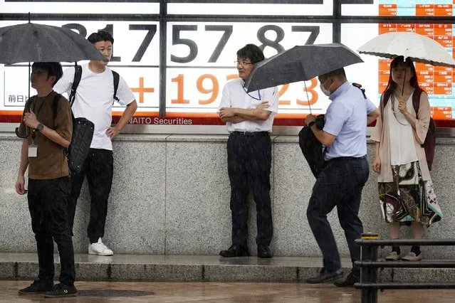 People stand in the rain in front of an electronic stock board showing Japan's Nikkei 225 index at a securities firm Tuesday, August 22, 2023, in Tokyo. (Photo by Eugene Hoshiko/AP Photo)