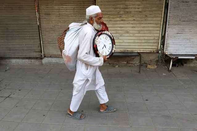 A man carrying wall-clocks for sale walks along closed currency exchange shops, in Peshawar, Pakistan on September 12, 2023. (Photo by Fayaz Aziz/Reuters)