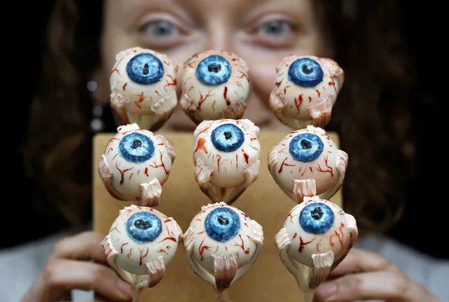 Cake Artist Sarah King displays her eyeball cakes at the “Feed the Beast extreme cake shop” in London, Thursday, October 24, 2013. The Halloween themed cake shop will have a 6ft long devil horse cake dripping blood, and the giant rotting maggot riddled section of a Kraken eye. Smaller items include rotting chocolate hands and feet, wound cupcakes and maggot topped gluten free cupcakes, it is open at The Rag Factory near Brick Lane in London on October 26 and 27. (Photo by Kirsty Wigglesworth/AP Photo)