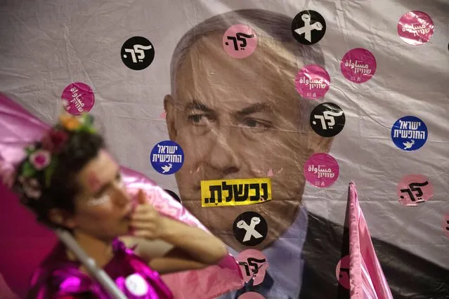 An Israeli protester wears pink during a demonstration against Israeli Prime Minister Benjamin Netanyahu outside his official residence in Jerusalem, Saturday, June 12, 2021. If all goes according to plan, Israel will swear in a new government on Sunday, ending Prime Minister Benjamin Netanyahu's record 12-year rule and a political crisis that inflicted four elections on the country in less than two years. Hebrew reads: “You failed”, “Israel free” and “Leave”. (Photo by Ariel Schalit/AP Photo)