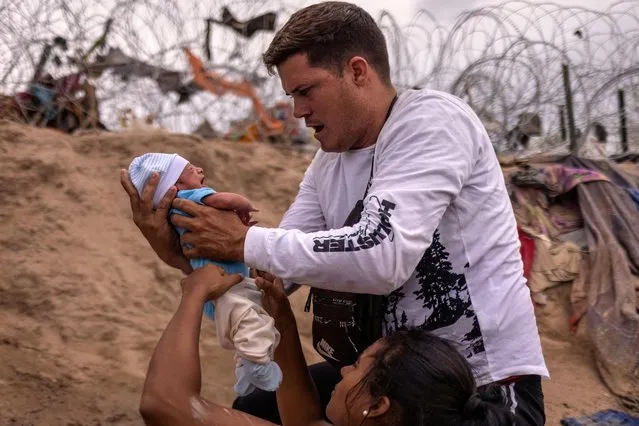 Yusniel, a 34 year old migrant from Cuba, holds his ten-day-old son Yireht, who is being dressed by his mother Yanara, 30, during a diaper change as the family searched for an entrance past the wire fence along the banks of the Rio Grande river after wading into the United States from Mexico, in Eagle Pass, Texas, U.S., October 6, 2023. (Photo by Adrees Latif/Reuters)