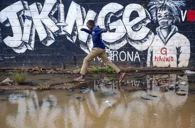 A boy steps across a flooded area next to an informational mural with words in Swahili advising people to protect themselves from the coronavirus and get vaccinated, in the low-income Kibera neighborhood of Nairobi, Kenya, Saturday, June 12, 2021. Africa's 1.3 billion people account for 18% of the world's population. But the continent has received only 2% of all vaccine doses administered globally. (Photo by Brian Inganga/AP Photo)