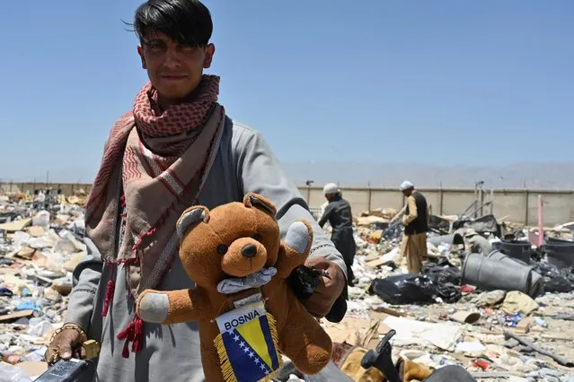In this picture taken on June 17, 2021, a man holds a teddy bear as people look for useable items at a junkyard near the Bagram Air Base in Bagram. The Pentagon is evacuating Bagram airbase as part of its plan to withdraw all forces by this year's 20th anniversary of the September 11 attacks on the US, taking military gear home or given to Afghan security forces, but tons of civilian equipment must be left behind. (Photo by Adek Berry/AFP Photo)