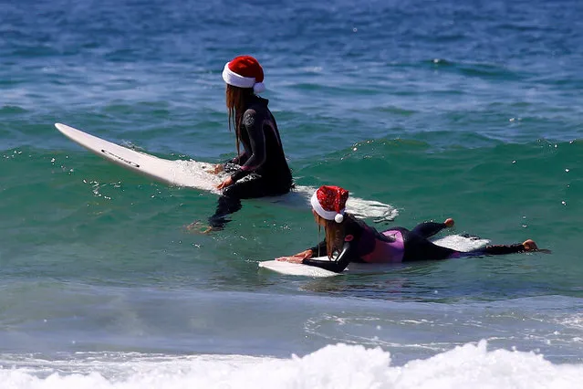 German tourists Mimi Wiebeling (R) and Pauline Lapetite sit on their surfboards as they wear Christmas hats at Sydney's Bondi Beach on Christmas Day in Australia, December 25, 2016. (Photo by David Gray/Reuters)