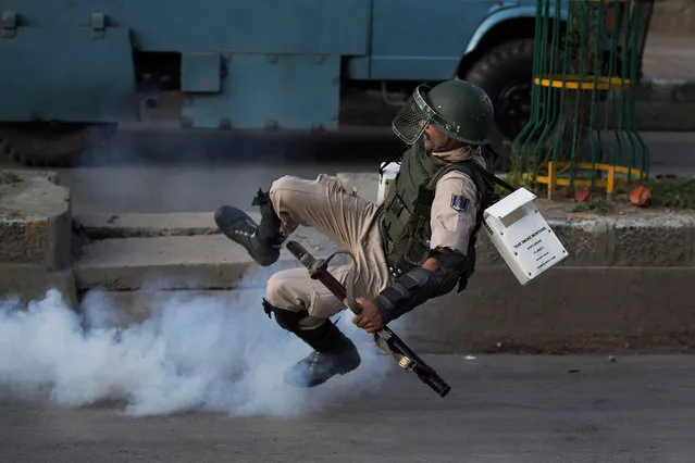 An Indian paramilitary soldier falls down as he tries to kick back an exploded tear gas shell thrown back at them by Kashmiri Muslim protesters at the end of a day long curfew in Srinagar, Indian controlled Kashmir on August 8, 2016. Kashmir has been under a security lockdown and curfew since the killing of a popular rebel commander on July 8 sparked some of the largest protests against Indian rule in recent years. (Photo by Dar Yasin/AP Photo)