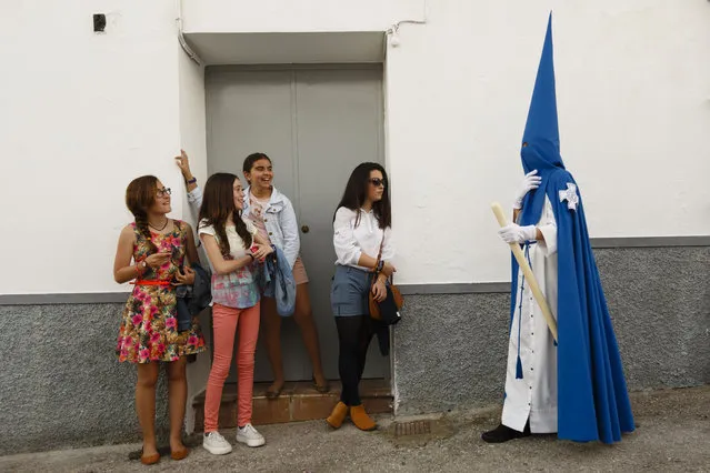 Girls look at a penitent taking part in “Nuestro Senor Atado a la Columna, Maria Santisima de la Paz y San Juan Evangelista” Holy Week procession in Arcos de la Frontera, Spain, Tuesday, March 31, 2015. Hundreds of processions take place throughout Spain during the Easter Holy Week. (Photo by Daniel Ochoa de Olza/AP Photo)