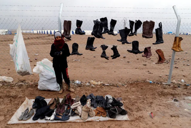 A displaced Iraqi boy who fled the Islamic State stronghold of Mosul, is selling second-hand shoes following heavy rain at Khazer camp, Iraq, December 19, 2016. (Photo by Ammar Awad/Reuters)
