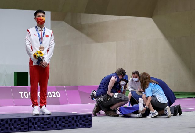 Bronze medallist Yang Haoran of China stands on the podium as a volunteer receives medical attention during  a medal ceremony for the men's 10m air rifle final during the Tokyo 2020 Olympic Games at the Asaka Shooting Range in the Nerima district of Tokyo on July 25, 2021. (Photo by Ann Wang/Reuters)