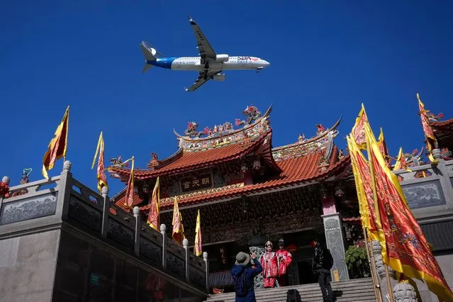 A Shandong Airlines plane flies over a pair of newly weds as they pose for wedding photos at a Chaotian Palace Temple in Xiamen in southeast China's Fujian province, Monday, December 25, 2023. (Photo by Andy Wong/AP Photo)