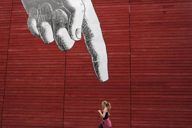 A woman runs past artwork of a large hand on a wall in central London, Britain April 27, 2015. (Photo by Stefan Wermuth/Reuters)