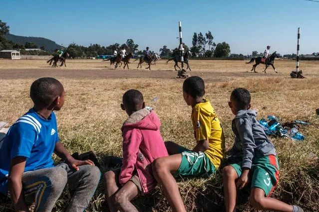 Children watch members of the Addis Ababa Polo Club as they practice at the Jan Meda Race Ground, in Addis Ababa on December 4, 2021. The club was founded in the 1940s, when it was part of the Imperial horse racing track. Today, it has a dozen members, and there are 3 other polo clubs in the city belonging to the security forces. (Photo by Eduardo Soteras/AFP Photo)