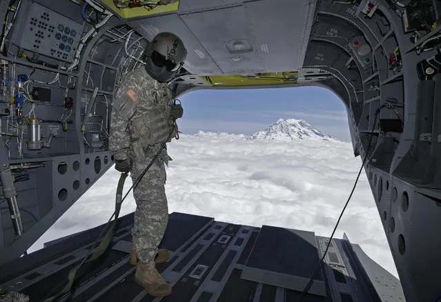 In this photo taken May 15, 2015, U.S. Army Reserve Staff Sgt. Ryan Elkins, a flight engineer, stands near the open rear door of a Boeing CH-47F Chinook helicopter as it flies near Mount Rainier in Washington state to give members of the media a view of mountain search and rescue training exercises involving another CH-47F. (Photo by Ted S. Warren/AP Photo)