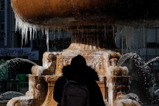 A pedestrian looks at a partially frozen fountain in New York, Tuesday, January 11, 2022. A mass of arctic air swept into the Northeast on Tuesday, bringing bone-chilling sub-zero temperatures and closing schools across the region for the second time in less than a week. (Photo by Seth Wenig/AP Photo)