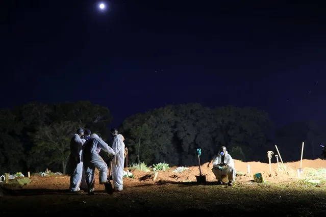 Gravediggers wearing protective suits rest between burials during the night at Vila Formosa cemetery in Sao Paulo, Brazil, March 30, 2021. As Brazil breaks a new record of daily COVID-19 deaths, cemeteries in the South American nation are holding funerals at night to accommodate all the burials. (Photo by Amanda Perobelli/Reuters)