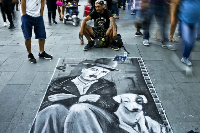 In this Sunday, March 12, 2017 photo, Daniel Maturana sits next to his drawing of Charlie Chaplin in hopes of tips from pedestrians in Plaza de Armas in downtown of Santiago, Chile. The downtown square is the capital's center, hosting municipal offices, the Cathedral, the post office and colorful personalities from artists to street preachers. (Photo by Esteban Felix/AP Photo)
