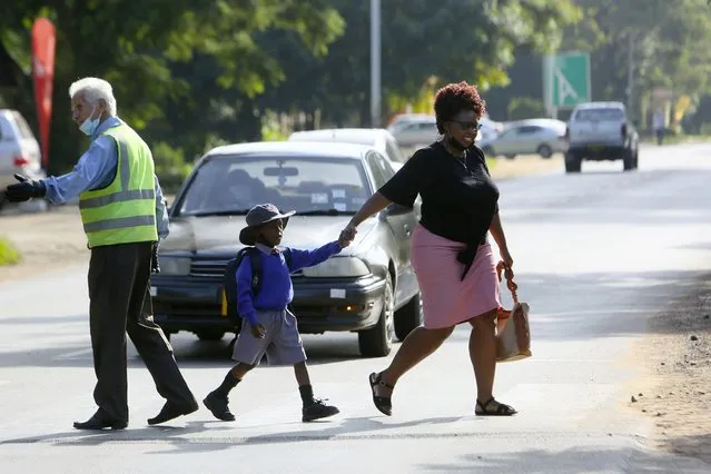A parent crosses the road with her child on her way to school in Harare, Wednesday, February 9, 2022. (Photo by Tsvangirayi Mukwazhi/AP Photo)