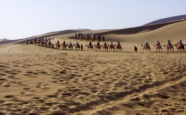 Tourists riding camels visit Mingsha Mountain and Crescent Spring scenic spot on June 27, 2024 in Dunhuang, Gansu Province of China. (Photo by Bao Kangxuan/VCG via Getty Images)