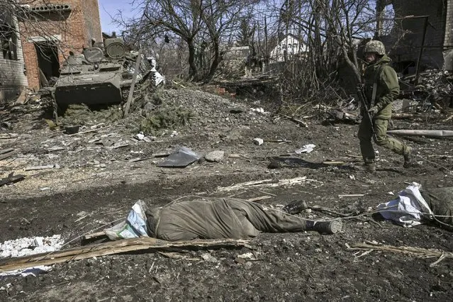 A man walks past a body of a Russian soldier laying on the ground after the Ukranian troops retaking the village of Mala Rogan, east of Kharkiv, on March 28, 2022. (Photo by Aris Messinis/AFP Photo)