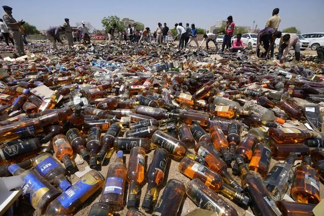 Indian laborers arrange seized liquor bottles to destroy them as police officials and media persons watch in Ahmedabad, Gujarat state, India, Wednesday, March 30, 2022. Police officials destroyed thousands of seized illegal liquor bottles in this western state where liquor is prohibite. (Photo by Ajit Solanki/AP Photo)