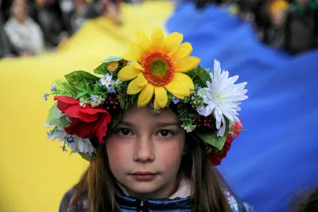 A young girl looks at a camera as people carry a huge Ukrainian flag as they participate in a peaceful demonstration “Solidarity with Ukraine” in Krakow, Poland, April 24, 2022. (Photo by Jakub Wlodek/Agencja Wyborcza.pl via Reuters)