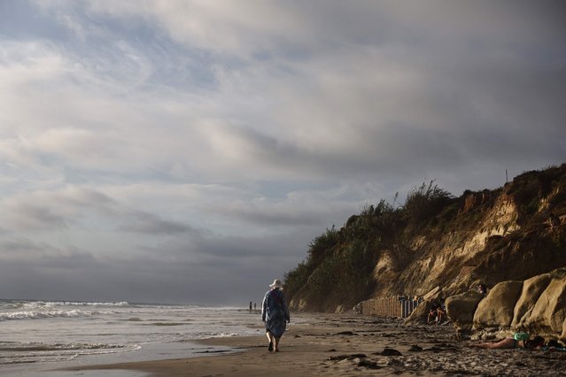 A person walks at high tide along eroding bluffs which help support the Amtrak Pacific Surfliner rail corridor along the Pacific Ocean coastline on August 16, 2024 in Del Mar, California. Rising sea levels and stronger storms have contributed to increased erosion and landslides along the vital Amtrak Pacific Surfliner coastal rail corridor which runs over 350 miles through Southern California to California's Central Coast. Erosion and landslides on coastal bluffs led to three extended closures along the route in 2023 and 2024 and twelve shutdowns in the past six years. With climate change expected to bring more intense storms and higher seas, most officials believe vulnerable sections of the corridor will need to be moved inland. The scenic route is the second-most popular Amtrak corridor in the country and also serves commuter and freight trains. (Photo by Mario Tama/Getty Images/AFP Photo)