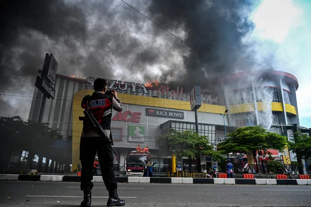 A police officer take photos as firefighters respond at a shopping mall after a fire broke out with no casualties reported, in Banda Aceh on April 4, 2022. (Photo by Chaideer Mahyuddin/AFP Photo)