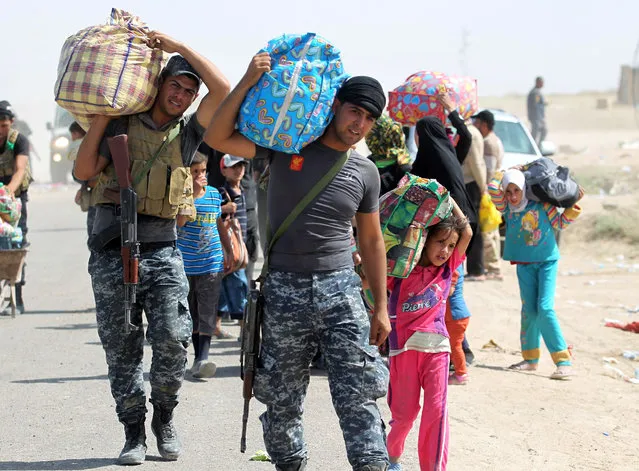 Members of the Iraqi government forces help people who fled the violence in their village of Saqlawiyah, north west of Fallujah, carry their belongings at a military point outside their village, on June 3, 2016. Iraqi forces launched an offensive a week ago to recapture Fallujah, which became an Islamic State group stronghold after its fighters seized the city in January 2014. (Photo by Ahmad Al-Rubaye/AFP Photo)