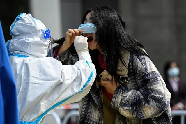A health worker takes a swab sample from a woman at a Covid-19 coronavirus testing site outside office buildings in Beijing on April 29, 2022. (Photo by Jade Gao/AFP Photo)