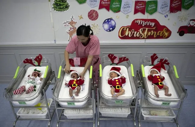 A nurse adjusts the outfits of newborn babies dressed in Santa costumes on Christmas eve at the Synphaet hospital in Bangkok, Thailand, Tuesday, December 24, 2019. (Photo by Sakchai Lalit/AP Photo)
