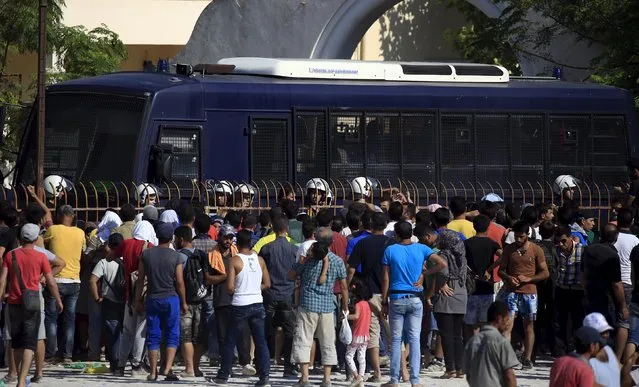 Greek riot police stand guard in front of a police bus as migrants and refugees wait to be registered at the national stadium of the island of Kos, August 12, 2015. (Photo by Alkis Konstantinidis/Reuters)