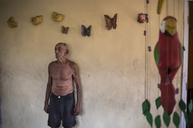 Jose Calderon, 86, stands next to wall adornments given to him by neighbors in “Los Hijos de Dios” neighborhood in Maracaibo, Venezuela, Wednesday, November 20, 2019. Few in Maracaibo have responded to Venezuelan opposition leader Juan Guaido's efforts to reignite his movement, despite it being a city hard hit by crisis. Its residents endure daily power outages in a region that’s punishingly hot. (Photo by Rodrigo Abd/AP Photo)