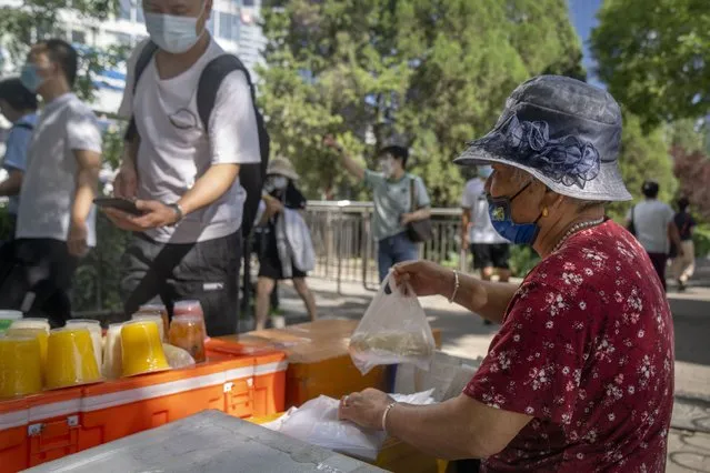 A vendor wearing a face mask sells snacks along a street in the central business district in Beijing, Thursday, July 7, 2022. (Photo by Mark Schiefelbein/AP Photo)