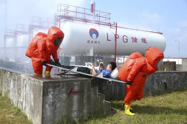 Firefighters in protection suits carry a a man playing the role of a victim on a stretcher during an anti-chemical drill next to storage tanks of liquefied petroleum gas, at a factory in Haikou, Hainan province, China, August 21, 2015. (Photo by Reuters/Stringer)