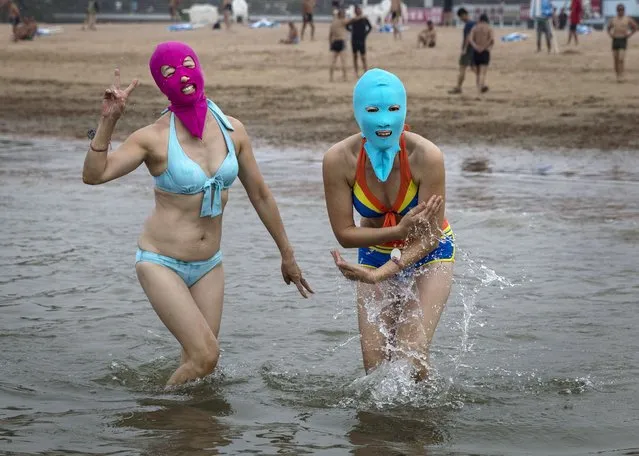Chinese women wear face-kinis as they walk in to the water to swim at the beach on August 20, 2014 in the Yellow Sea in Qingdao, China. The locally designed mask is worn by many local women to protect them from jellyfish stings, algae and the sun's ultraviolet rays. (Photo by Kevin Frayer/Getty Images)