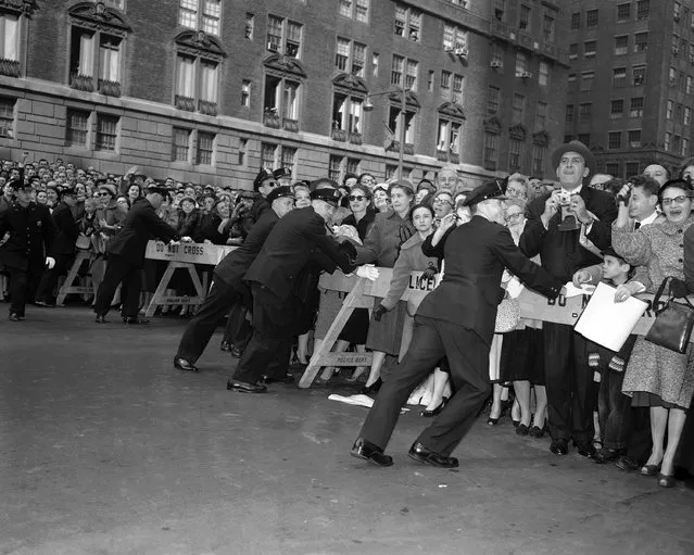 New York City policemen push against police stanchions at Park Avenue and 50th street, New York on October 21, 1957 in effort to contain crowd attempting to view Queen Elizabeth II as she drove to the hotel Waldorf-Astoria. (Photo by AP Photo)