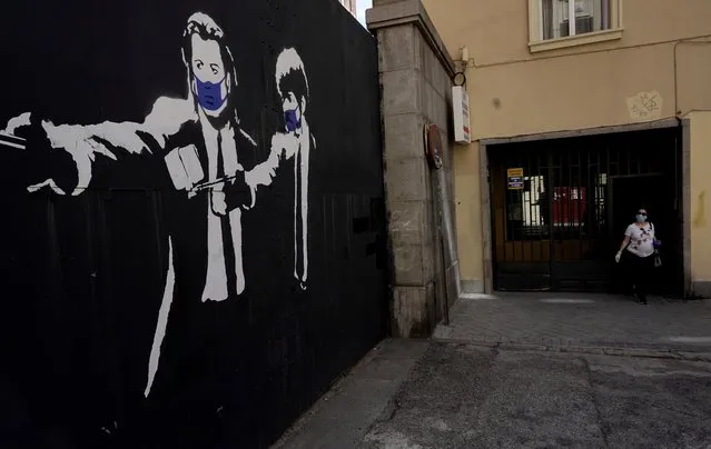 A woman leaves a building next to a graffiti showing actors from the movie “Pulp Fiction” John Travolta and Samuel L. Jackson wearing protective masks, during the coronavirus disease (COVID-19) outbreak, in Madrid, Spain on May 3, 2020. (Photo by Juan Medina/Reuters)