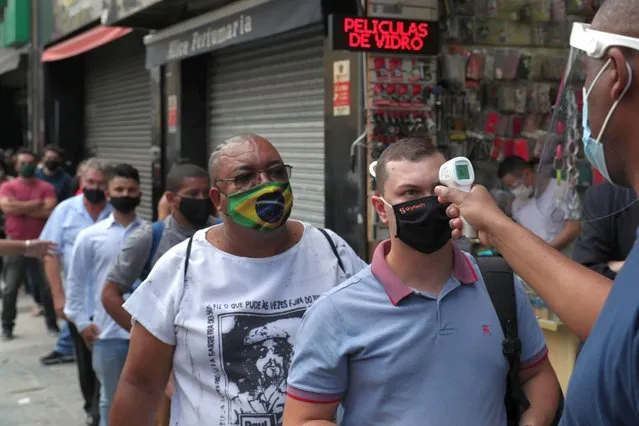 A man has his temperature checked as others queue to enter a popular mall that has reopened for the first time since the beginning of quarantine, as the city eases restrictions imposed to curb the spread of the coronavirus disease (COVID-19), in Sao Paulo, Brazil, June 11, 2020. (Photo by Amanda Perobelli/Reuters)