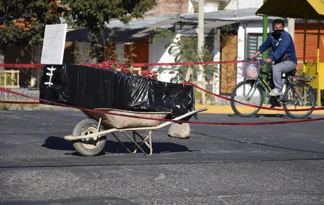 A coffin wrapped in plastic containing the remains of an unidentified men, who died last week, sits on a wheelbarrow in the middle of a street, placed there by his family to draw attention of the authorities to show that his remains are yet to be collected, in Cochabamba, Bolivia, Saturday, July 4, 2020. Funeral services in Cochabamba are overwhelmed and bodies are piling up, waiting for cremation or burial, as new coronavirus cases rapidly multiply in one of the epicenters of the pandemic in Bolivia. (Photo by Dico Soliz/AP Photo)