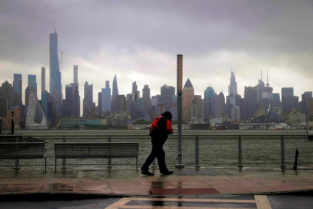 A man walks into heavy wind and rain along the waterfront of the Hudson River in front of the New York City skyline during Tropical Storm Isaias in Weehawken, New Jersey, August 4, 2020. (Photo by Mike Segar/Reuters)