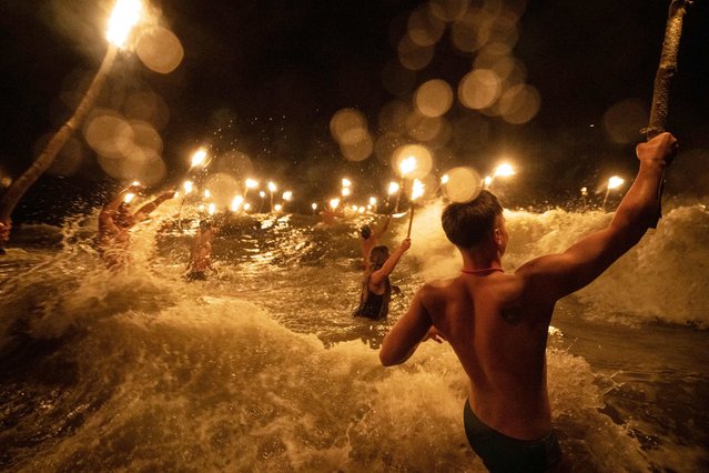 Lifeguards carry torches as they wade into the ocean in a ceremony to commemorate Lifeguard Day, to honor their commitment to safety and aquatic rescue, in Mar Azul, Argentina, Wednesday, February 14, 2024. (Photo by Rodrigo Abd/AP Photo)