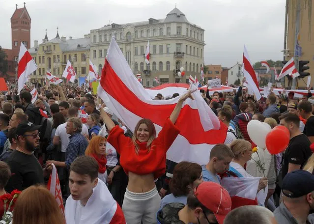 A woman holds a historical flag of Belarus during a protest in Minsk, Belarus, Sunday, August 23, 2020. More than 100,00 protesters demanding the resignation of Belarus' authoritarian president are rallying in a vast square in the capital, continuing the massive outburst of dissent that has shaken the country since dubious presidential elections two weeks ago. (Photo by Sergei Grits/AP Photo)