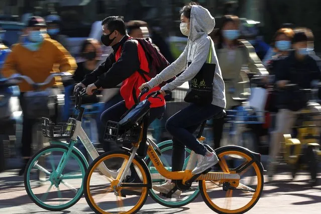 People wearing face masks to help curb the spread of the coronavirus ride bicycle during the morning rush hour in Beijing, Monday, October 12, 2020. Even as China has largely controlled the outbreak, the coronavirus is still surging across the globe with ever rising death toll. (Photo by Andy Wong/AP Photo)