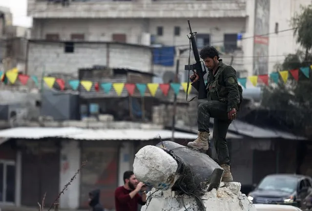 A Turkish-backed Syrian Arab fighter stands on a fallen statue of “Kawa” the blacksmith, who was a central figure in a Kurdish legend about the new year celebration of Noruz, in Afrin after they seized control of the northern Syria city from the Kurdish People's Protection Units (YPG) on March 18, 2018. In a major victory for Ankara's two-month operation against the Kurdish People's Protection Units (YPG) in northern Syria, Turkish-led forces pushed into Afrin apparently unopposed, taking up positions across the city. (Photo by Omar Haj Kadour/AFP Photo)