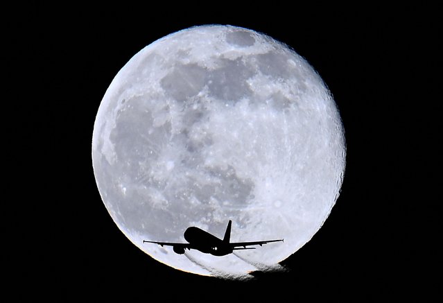 An aircraft passes in front of the moon as it flies over London, Britain on February 6, 2023. (Photo by Toby Melville/Reuters)