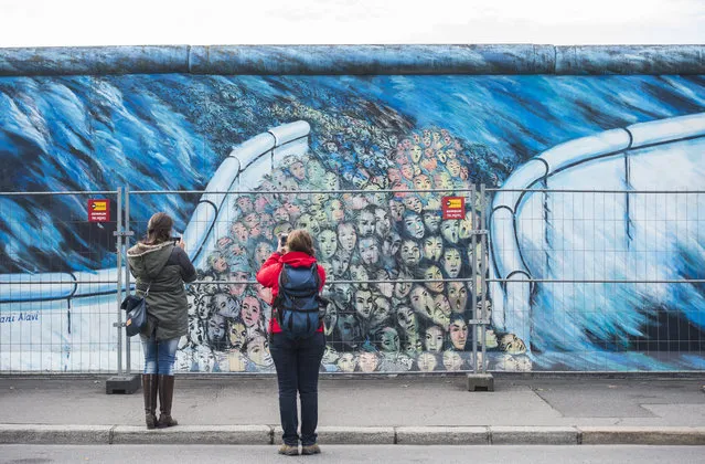 A temporary fence protects wall paintings on the East Side Gallery, a much-visited stretch of the Berlin wall, while graffiti-cleaning work is underway in Berlin on November 5, 2015. The city of Berlin has decided to erect a 80cm high permanent barrier to discourage people from defacing the works made by artists who decorated the yet untouched east side with artwork and political statements after the wall was taken down in 1989-1990. (Photo by John Macdougall/AFP Photo)
